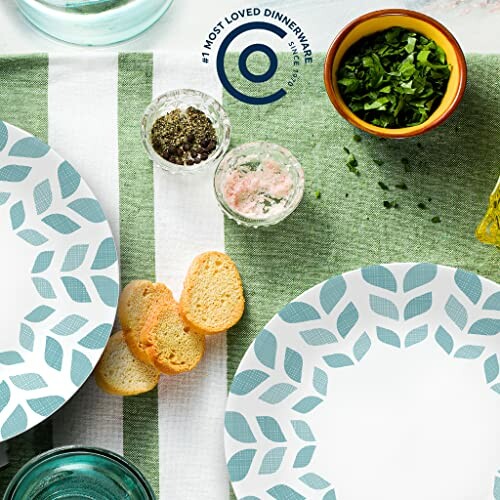 Dinnerware set on green cloth with herbs and bread.