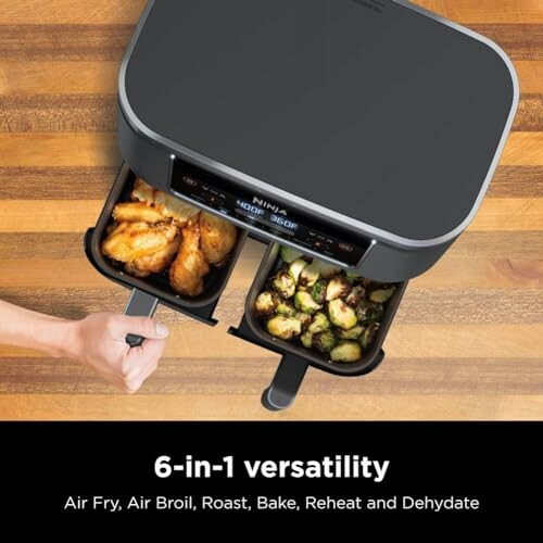 Ninja air fryer with cooked chicken wings and vegetables in trays.