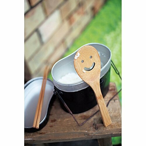 Wooden spoon with a smiley face next to a pot of rice.